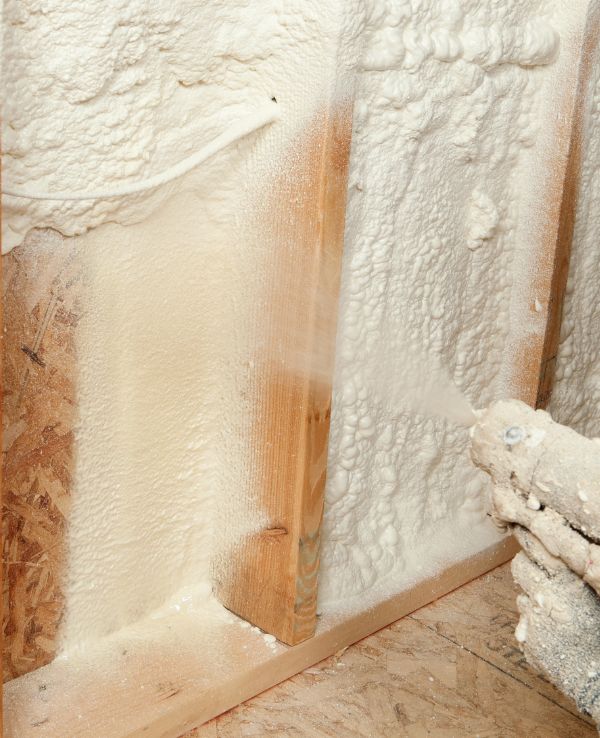 A man uses a spray nozzle to apply foam insulation to a wall, demonstrating a home improvement technique.