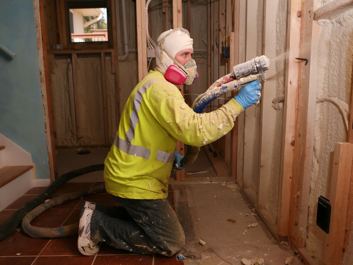 A man wearing a safety vest and helmet is actively working on a wall, focusing on his task with tools in hand.
